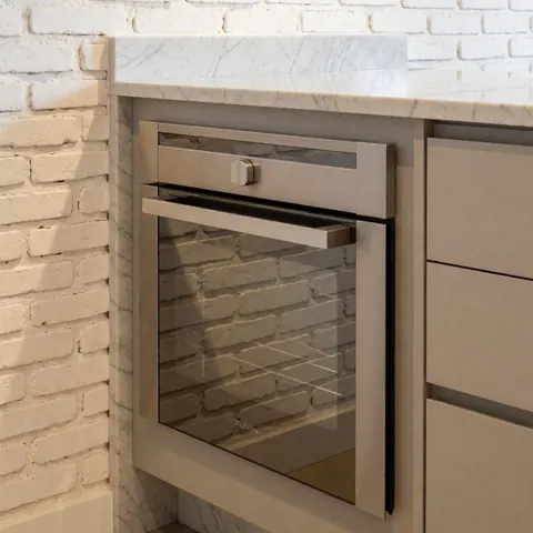 Un four en acier inoxydable est intégré dans une île de cuisine avec un plan de travail en marbre blanc et un mur en briques peintes en blanc, reflétant la lumière ambiante.