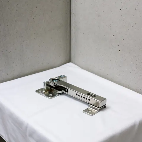 Nouveau mécanisme de charnière métallique et poli du réfrigérateur posé sur un tissu blanc avec des murs en béton lisse et un éclairage professionnel doux.