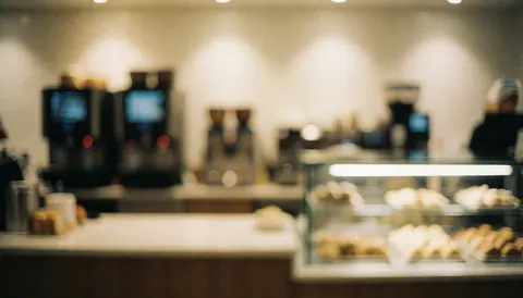 Fond flou d'une cafétéria avec machines à café et vitrine à pâtisseries, éclairage chaleureux, idéal pour ajouter du texte.