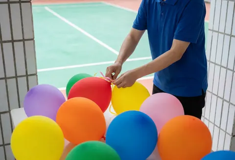 Un employé en chemise bleue prépare des ballons colorés sur un terrain extérieur pour décorer un événement.