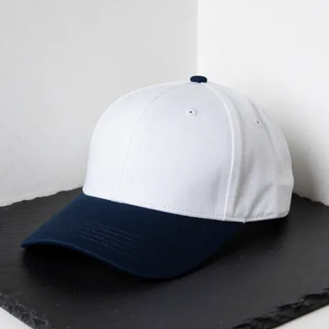 Casquette de baseball avec panneau avant blanc et visière bleu marine posée sur une surface en ardoise foncée, idéale pour personnalisation par broderie.