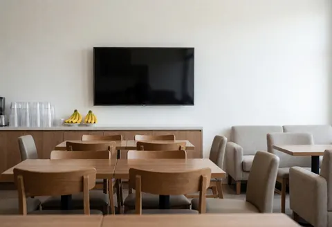 Espace d'attente spacieux équipé de tables en bois, de chaises confortables, d'une télévision et d'un plateau de fruits, idéal pour un club sportif.