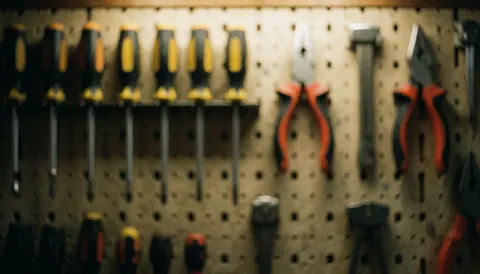 Fond flou d'outils accrochés sur un mur à clous, incluant des tournevis et des pinces, éclairage chaleureux, idéal pour des textes commerciaux.