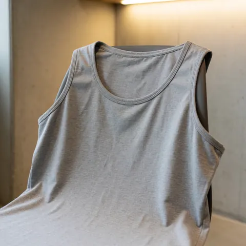 Un t-shirt gris pour l'entraînement est suspendu sur une chaise en bois, avec une texture de coton doux visible et un éclairage chaleureux.