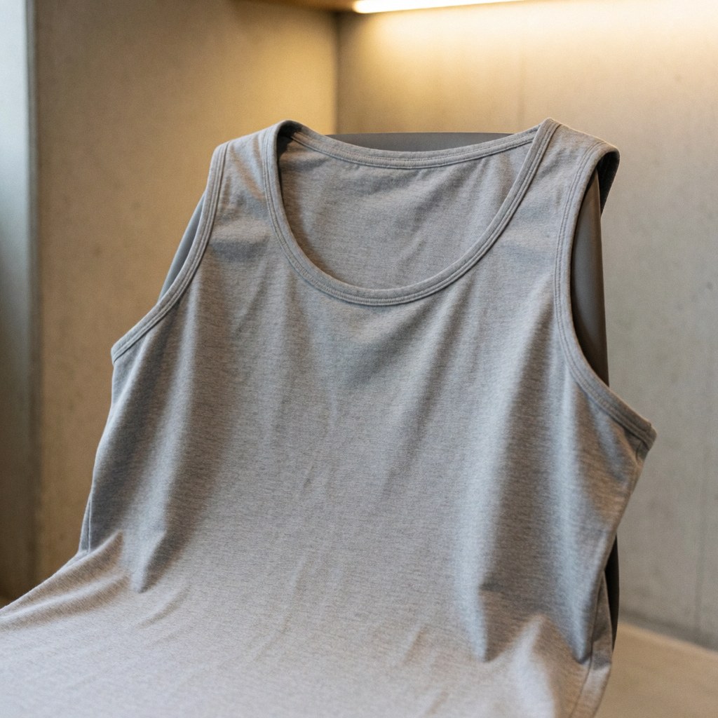 Un t-shirt gris pour l'entraînement est suspendu sur une chaise en bois, avec une texture de coton doux visible et un éclairage chaleureux.