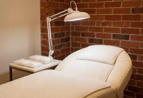 Lit de traitement blanc avec lampe ajustable sur mur en briques rouges, prêt pour un service professionnel.