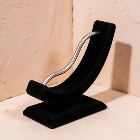 Barre de titane incurvée pour piercing posée sur un support en velours noir devant un mur terracotta clair avec un éclairage doux.