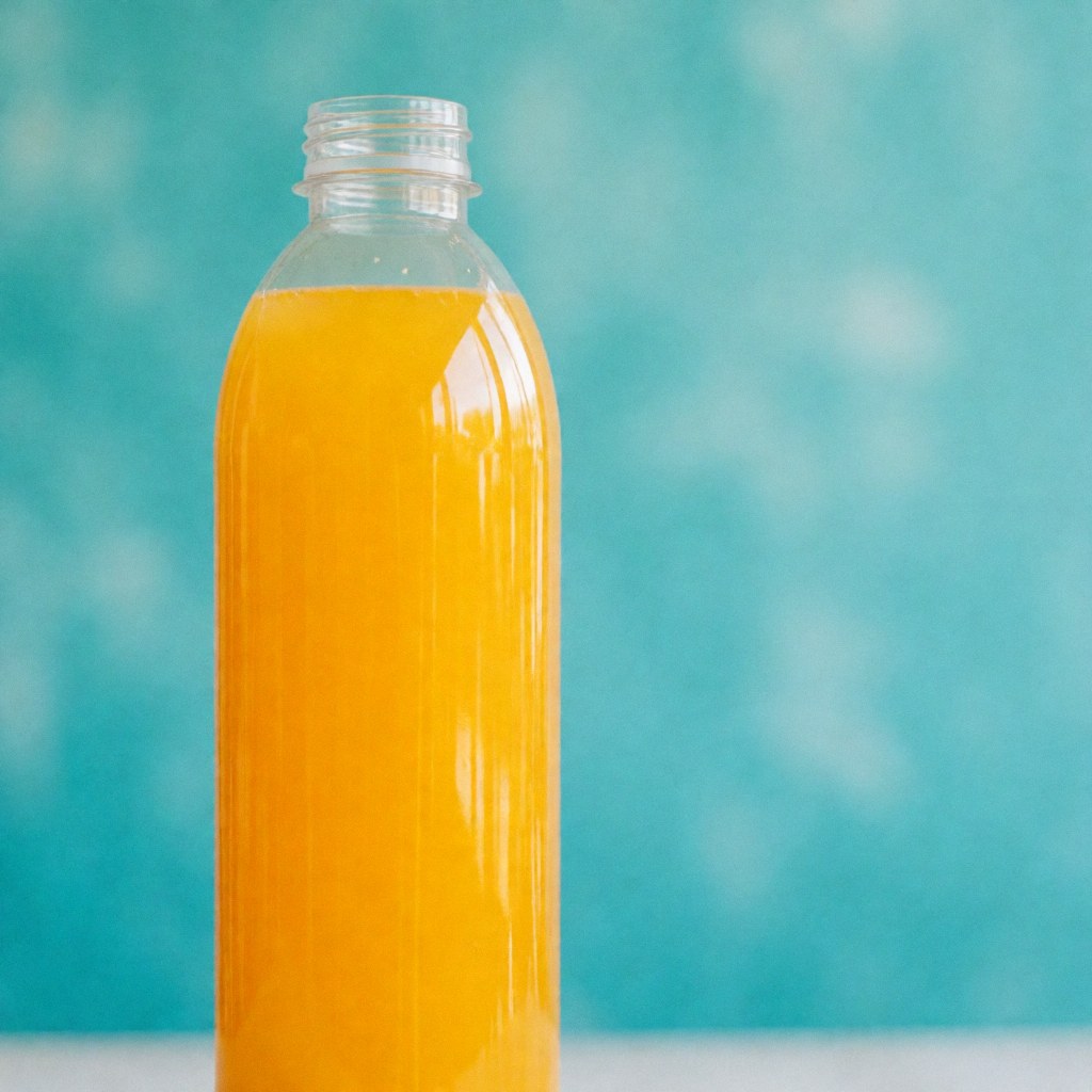 Bouteille transparente contenant du jus d'orange vif, posée sur un fond turquoise flou, idéale pour promouvoir des boissons rafraîchissantes dans les parcs aquatiques.