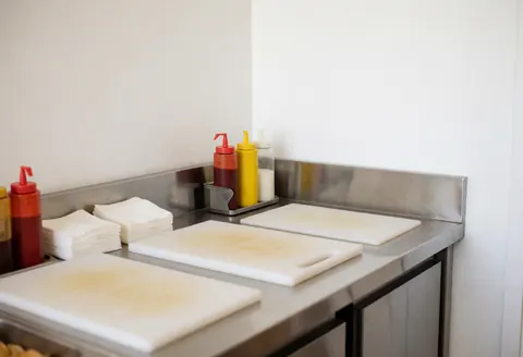 Station de préparation alimentaire avec des planches à découper, des distributeurs de sauce et des serviettes sur une cuisine en acier inoxydable.