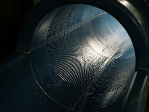 Vue intérieure d'un tube de toboggan aquatique en plastique bleu foncé, montrant la texture antidérapante, l'eau courante et les reflets sous un éclairage artificiel.