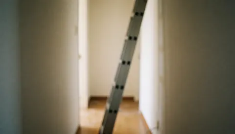 Échelle en aluminium posée contre un mur de couloir avec un fond flou, idéal pour superposer du texte publicitaire lié à la réparation des murs.