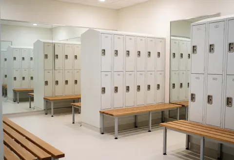 Vestiaire propre et ordonné avec des casiers blancs, des bancs en bois et des miroirs sur les murs, éclairage doux et professionnel.