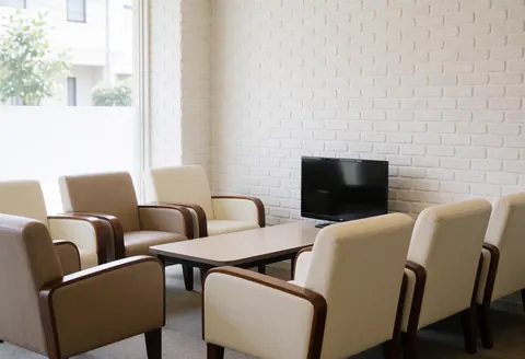 Espace d'attente aménagé avec des chaises confortables, une table basse et un téléviseur sur un mur en briques blanches baigné de lumière naturelle.
