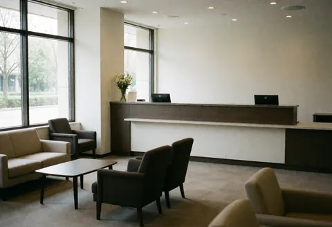Vue du hall d'un apparthotel contemporain incluant le bureau d'accueil équipé, une zone d'attente avec des canapés et des chaises, ainsi que de grandes fenêtres laissant entrer la lumière naturelle.