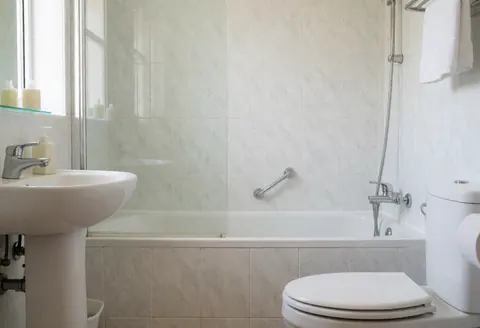 Salle de bain privée propre et moderne équipée d'une douche, d'un lavabo et d'un WC sur fond de carrelage clair.