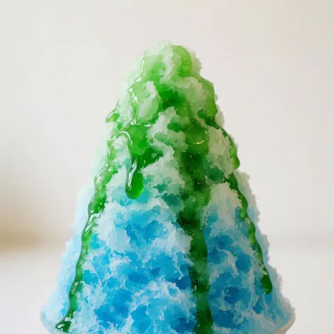 Glace bleue au granizo accompagnée d'une sauce verte brillante sur fond blanc doux, texture rafraîchissante.
