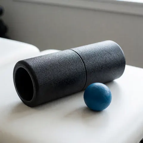 Rouleau de massage noir texturé et balle bleue posés sur une table blanche propre, idéaux pour la récupération musculaire et le bien-être en salle de sport.