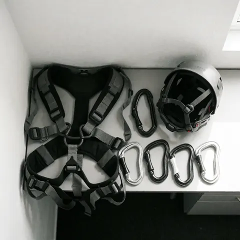 Vue de dessus d'un équipement professionnel d'escalade comprenant un harnais, un casque et des mousquetons disposés sur une surface blanche propre éclairée par la lumière naturelle.