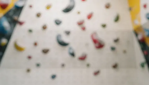 Fond de mur d'escalade intérieur avec des prises colorées floues, éclairage doux et neutre, idéal pour textes et design graphique.