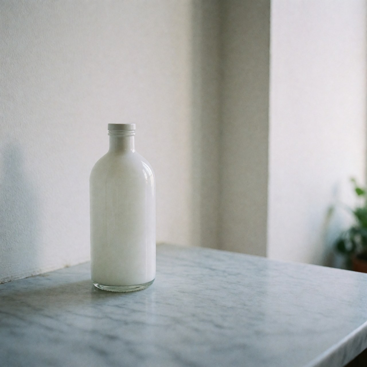 Flacon en verre blanc avec couvercle posé sur une table en marbre gris clair devant un mur blanc, éclairage naturel doux, sans personnes, idéal pour des produits de soin.