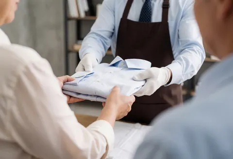 Une fourchette de chemise réparée est tenue entre les doigts, mettant en évidence les coutures visibles dans un atelier de couture au fond flou.