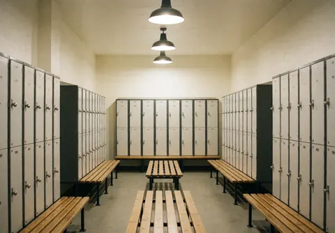 Vestiaire vide équipé de casiers métalliques et de bancs en bois, éclairé par des suspensions, prêt à accueillir les visiteurs.