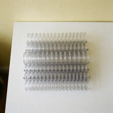 Des peignes de reliure en plastique transparent sont empilés en ligne sur une table blanche avec un fond crème, idéal pour les bureaux et les services de photocopie.