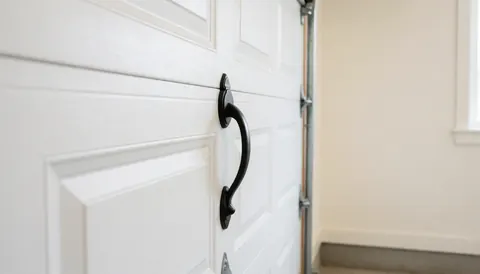 Porte de garage blanche munie d'une poignée noire, sur un mur clair. Scène propre et professionnelle, idéale pour les installateurs de portes de garage.