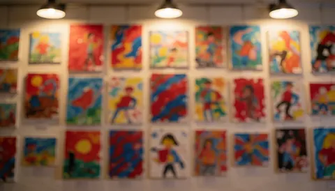 Fond de galerie avec plusieurs peintures abstraites pour enfants encadrées, éclairées par des lumières chaudes, idéal pour du texte.