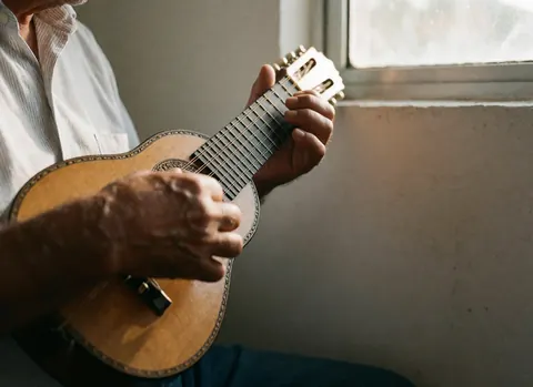 Gros plan sur des mains jouant d'un charango. Cordes et bois poli visibles sur fond blanc. Ambiance chaleureuse et professionnelle pour un atelier de théâtre.