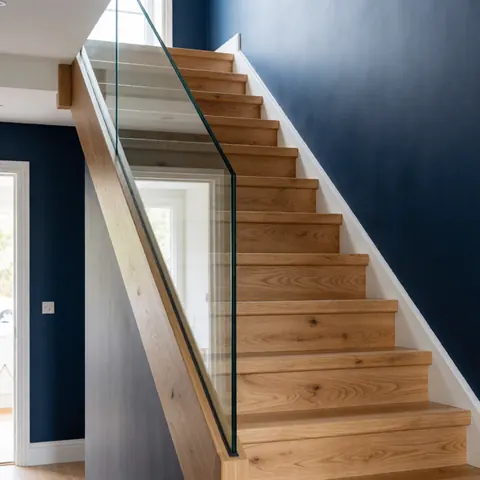 Escalier en chêne poli avec barrière en verre transparent, murs bleu foncé et lumière naturelle dans un couloir moderne.