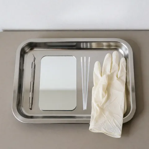 Plateau en acier inoxydable avec miroir, pince, cotons-tiges et gants en latex, prêt pour un service de lamination des sourcils dans un environnement hygiénique et professionnel.