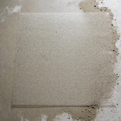 Une maille blanche en fibre de verre posée sur un sol gris avec des particules de poussière, préparation pour l'installation d'un plancher en liège.