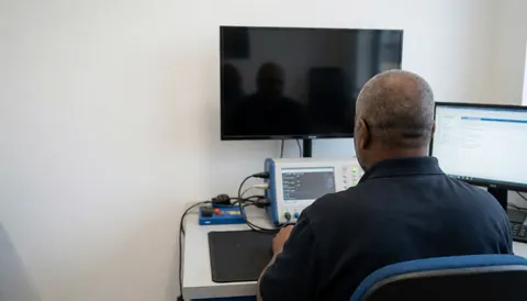 Un technicien professionnel examine un téléviseur à l'aide d'un équipement de diagnostic dans un atelier propre et bien éclairé, laissant un espace vide pour le texte.