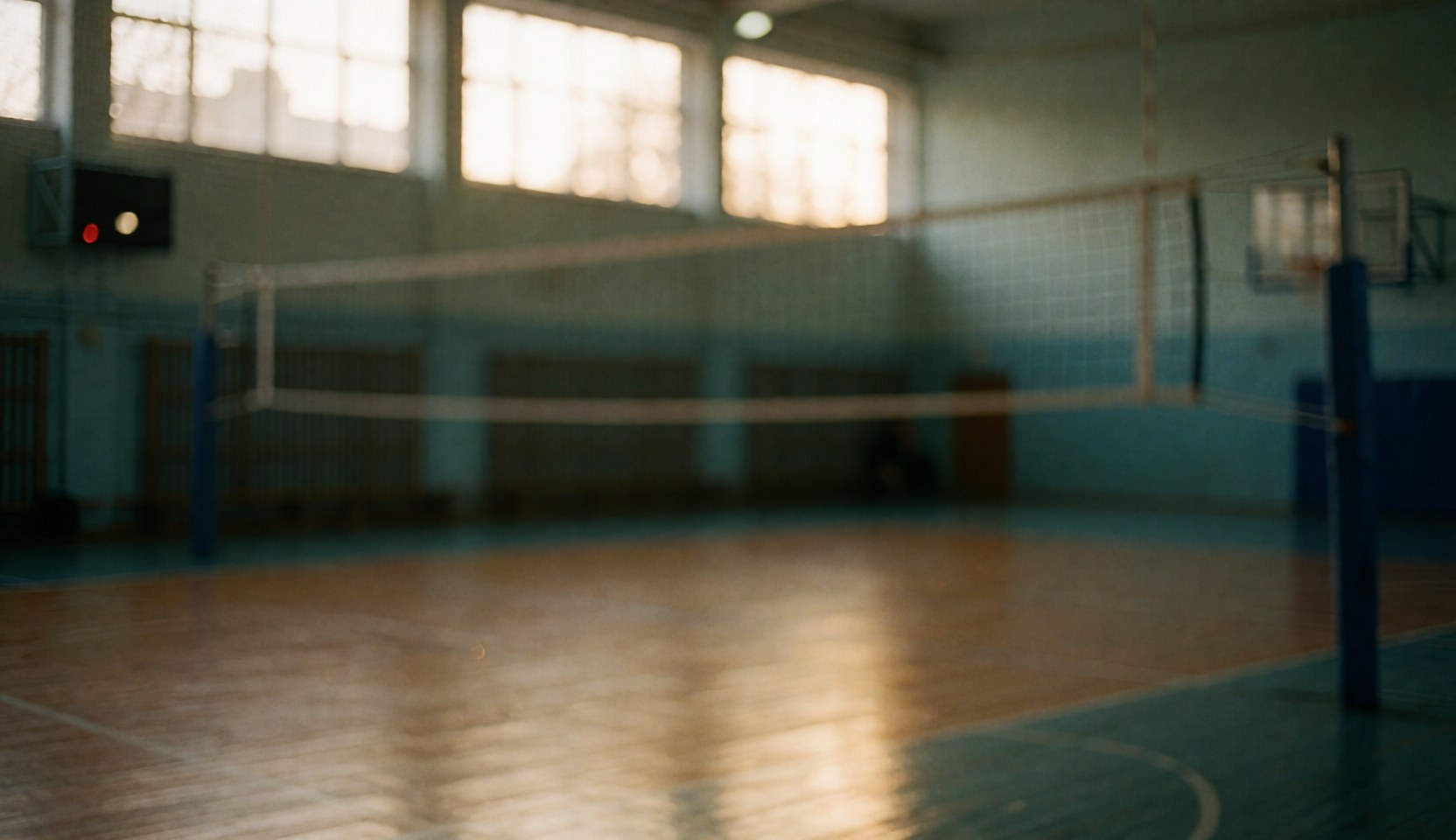 Fond flou d'un terrain de volley-ball intérieur avec filet, poteaux et sol en bois éclairé par une lumière chaude provenant de fenêtres hautes.