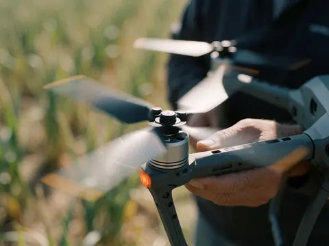Gros plan sur des mains tenant un drone avec hélices en rotation dans un champ agricole, illustrant la photographie aérienne de précision.