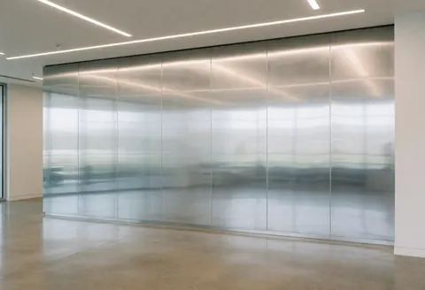 Mur en métal poli dans un bureau moderne, reflète les lumières linéaires du plafond, sol en béton poli, ambiance corporative vide et propre.
