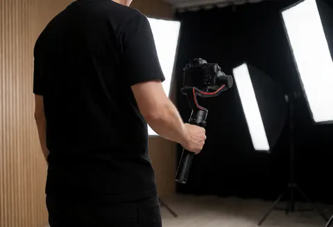 Photographe professionnel utilisant un gimbal et une caméra dans un studio équipé d'un softbox, d'un mur en bois et d'éclairages d'ambiance.