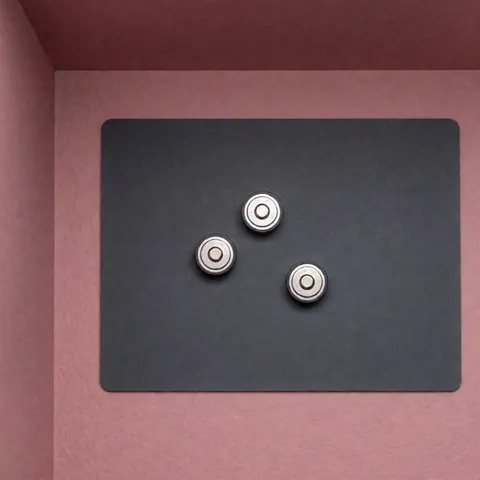 Trois piles bouton argentées posées sur un tapis antistatique gris, sur un fond rose pâle, pour la réparation de montres.