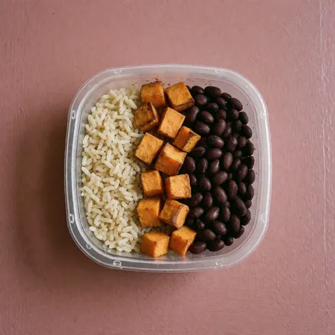 Vue de dessus d'un contenant de repas équilibré pour sportifs sur fond rose, contenant du riz, des haricots et de la patate douce.
