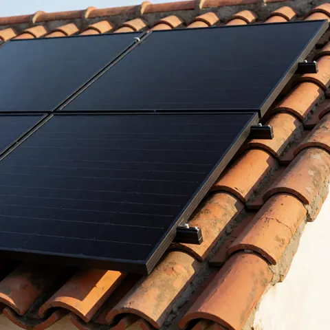 Panneau solaire noir installé sur un toit de tuiles terracotta avec une lumière solaire brillante et une texture céramique visible, montage sécurisé par des vis.