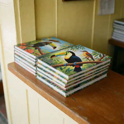 Une pile de livres éducatifs avec des illustrations d'oiseaux tropicaux posée sur un comptoir en bois poli dans un zoo.