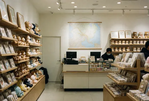 Intérieur d'une boutique de souvenirs avec étagères en bois, cartes murales et ours en peluche, un employé sert derrière le comptoir dans une ambiance chaleureuse.