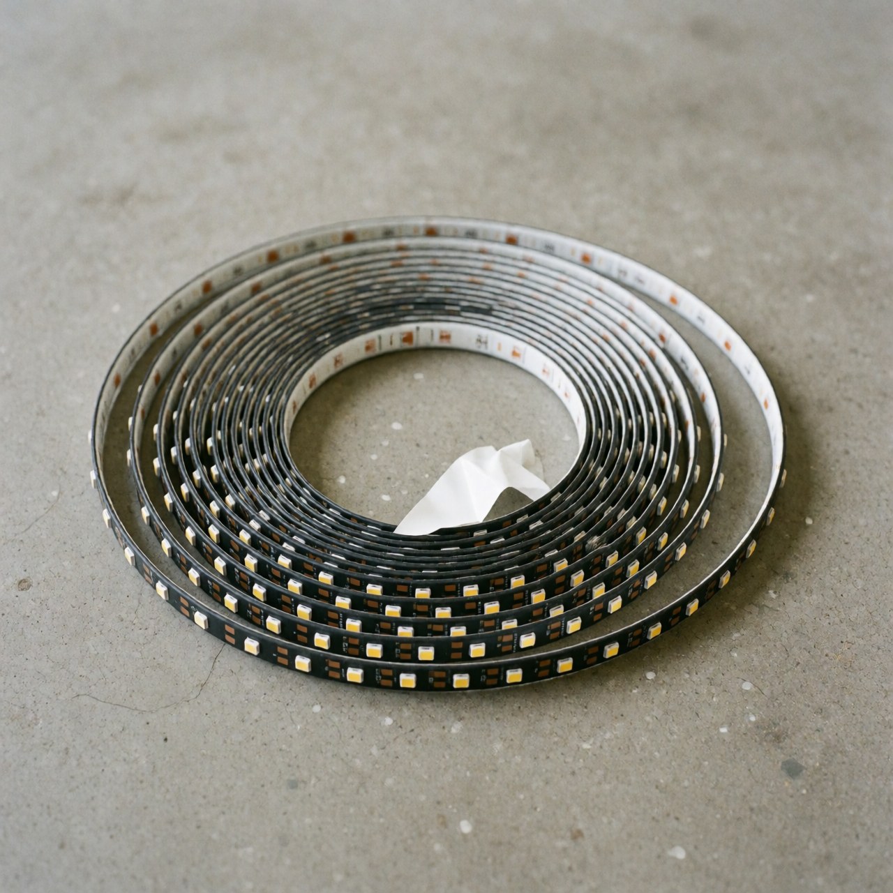Un ruban LED flexible avec adhésif est enroulé sur un sol en béton gris, idéal pour l'éclairage d'événements et la décoration.