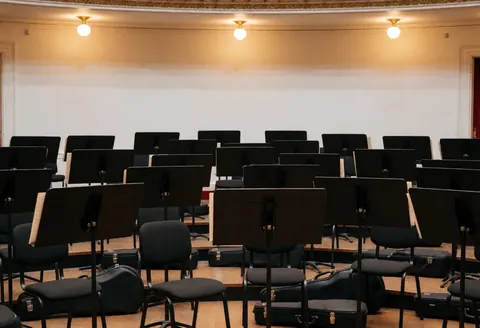 Fosse d'orchestre vide avec des pupitres noirs et des instruments de musique, éclairée par une lumière chaude dans un théâtre prêt pour un spectacle.