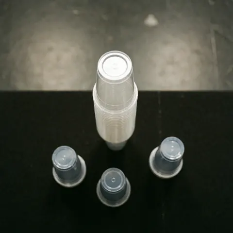 Gobelets en plastique empilés sur une surface noire mate, éclairage uniforme et flou d'arrière-plan pour événements ou restauration.