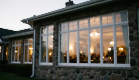 Façade en pierre du club de golf aux grandes fenêtres révélant une lumière chaleureuse et une ambiance accueillante au crépuscule.
