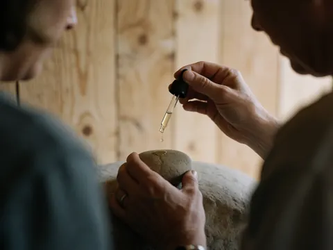 Des gouttes d'huile essentielle tombent sur une pierre avec des mains travaillant sur un fond en bois pour une scène de spa relaxante.