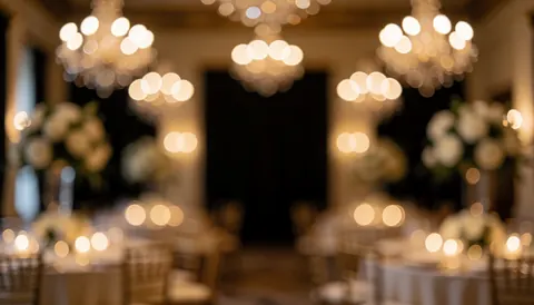 Fond désaturé d'une réception de mariage avec des lumières chaudes de chandeliers et bougies, tables et arrangements floraux, idéal pour du texte.
