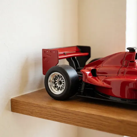 Maquette de voiture de course rouge avec détails de suspension et aileron arrière posée sur une étagère en bois éclairée par une lumière naturelle douce.